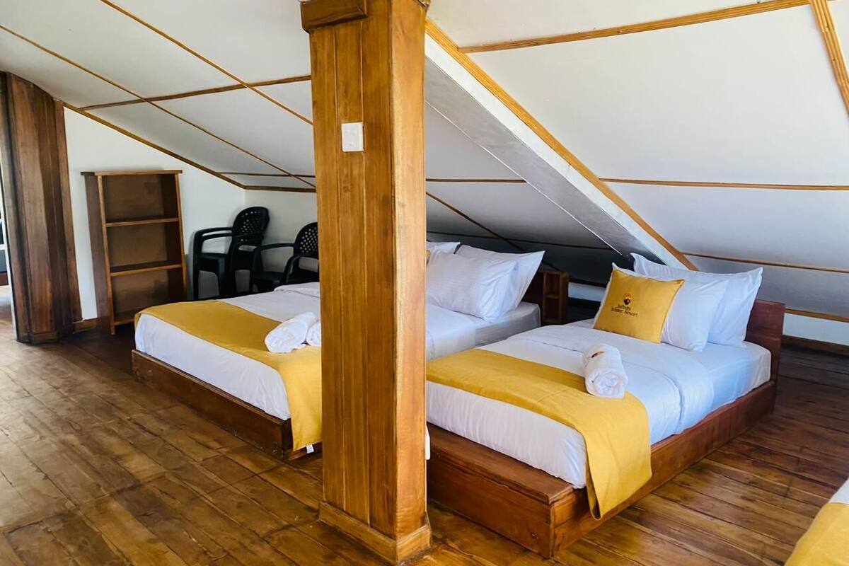Una habitación con dos camas, suelo de madera, un pilar de madera y techo inclinado.
