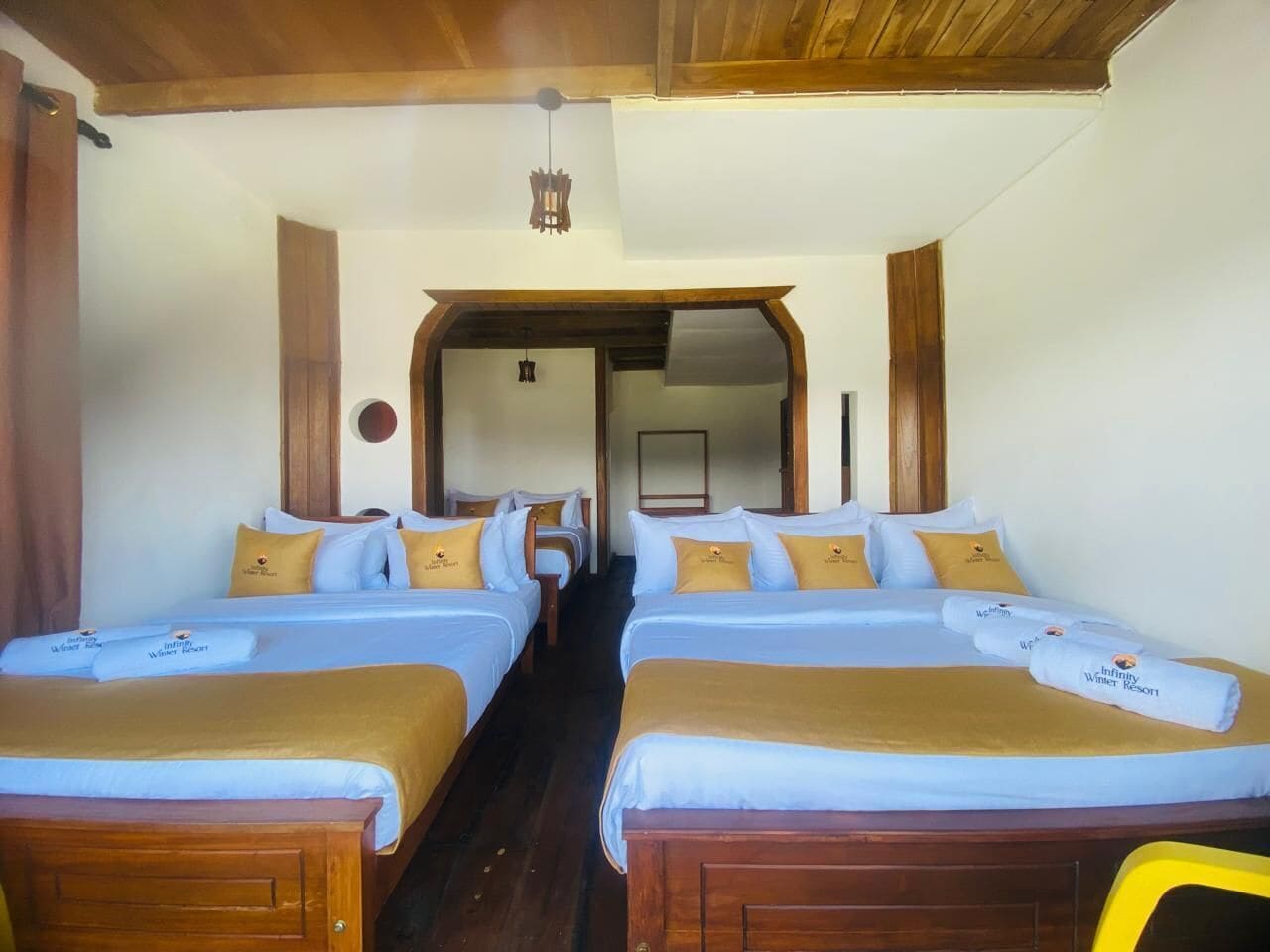 A hotel room with four beds arranged in a row, each with a wooden headboard and a blue bedspread.