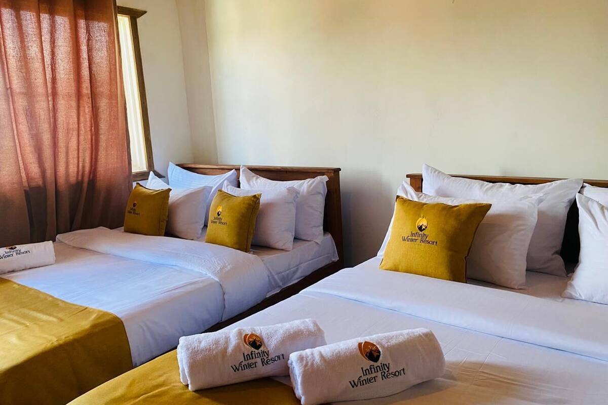 Habitación de hotel con dos camas, cada una con ropa de cama blanca y almohadas amarillas, y una mesa con toallas.