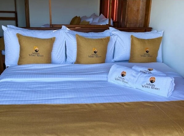 Un letto rifatto con biancheria bianca e marrone, due cuscini con un logo e un asciugamano piegato con lo stesso logo.