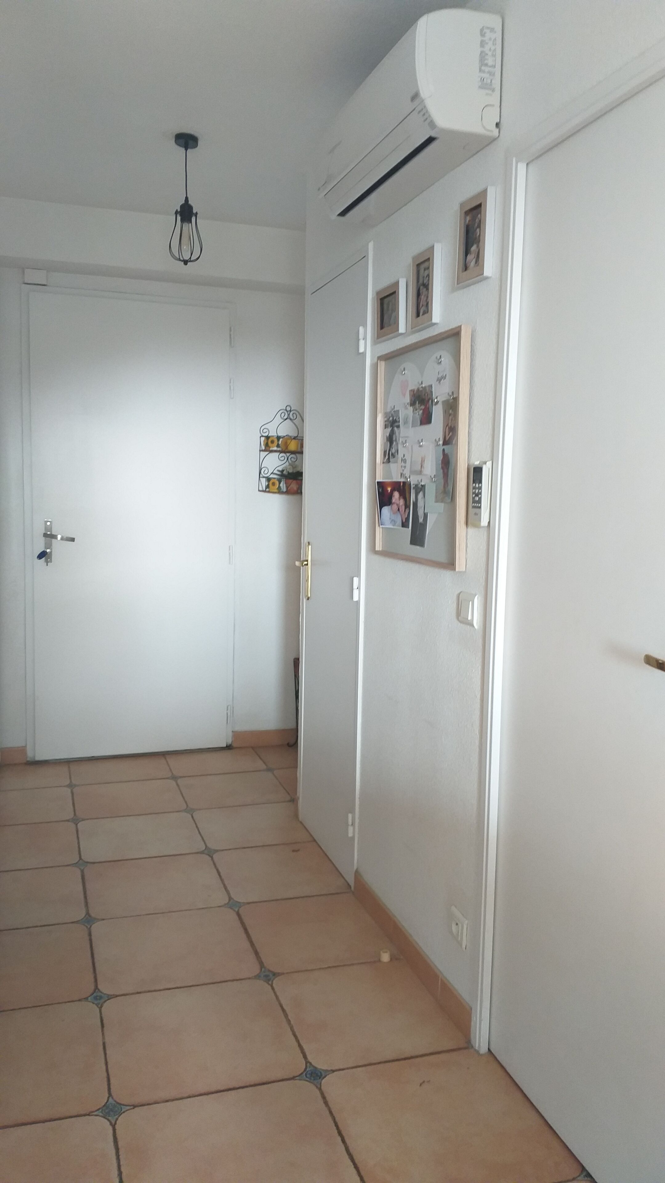 Ein Korridor mit gefliestem Boden, einer weißen Tür und einer Klimaanlage an der Wand.