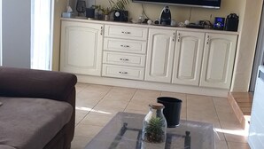 Olohuoneessa on sohva, lasinen sohvapöytä, jossa on koriste-esineitä, seinälle asennettu taulutelevisio ja valkoinen lipasto, jossa on laatikoita.