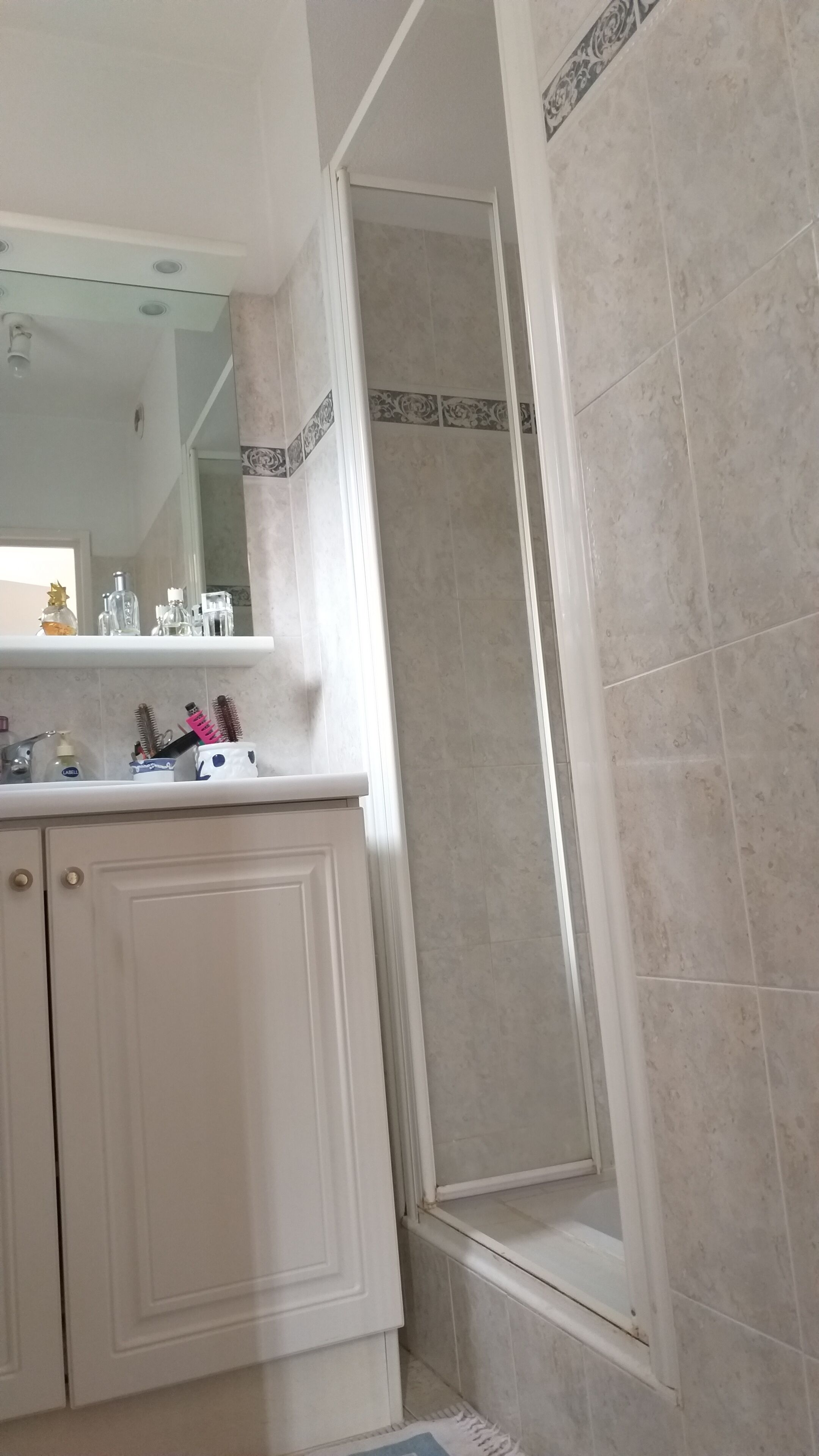 Een badkamer met een douche, een spiegel en een wastafel met toiletartikelen.