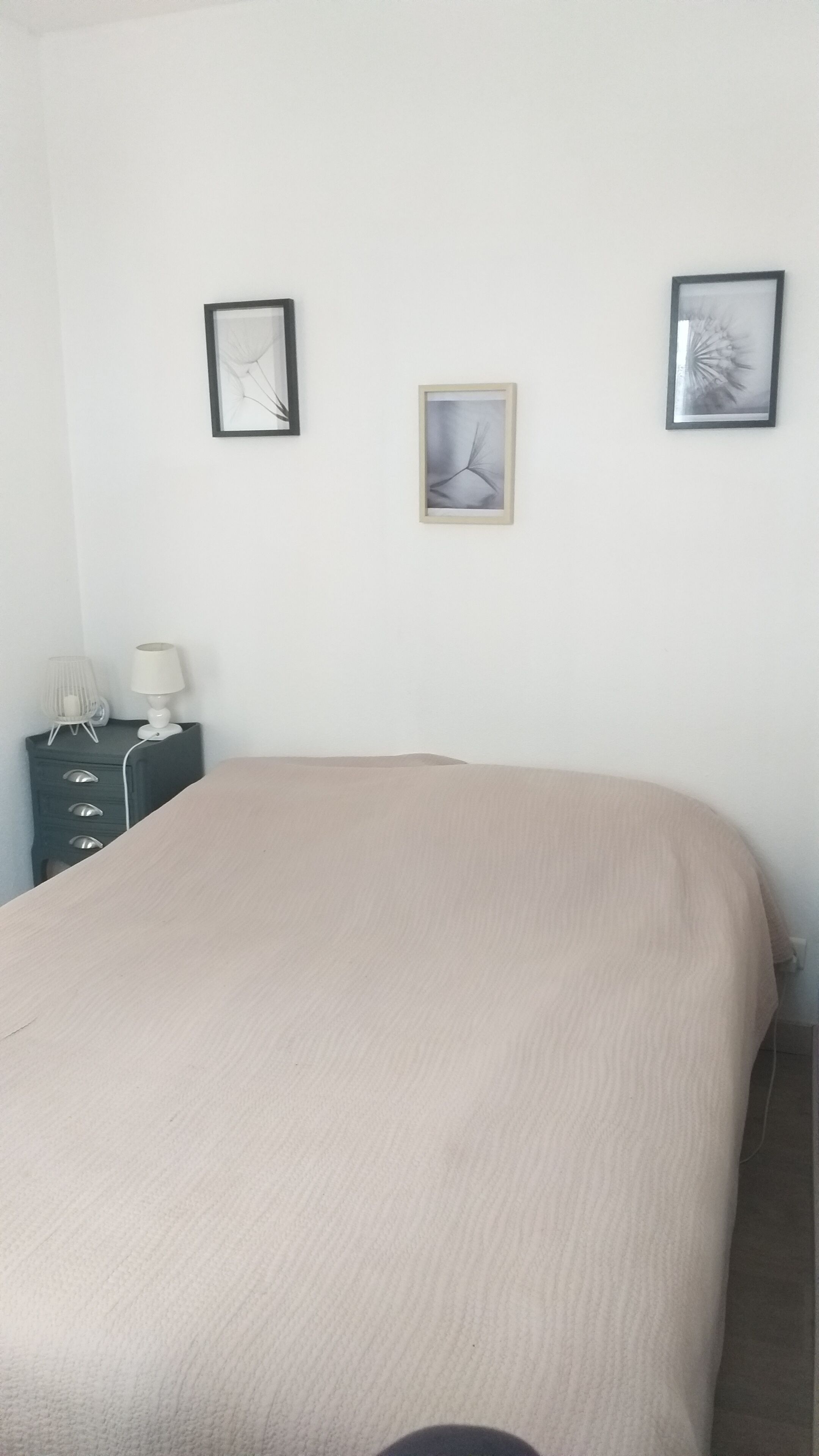 A bedroom with a bed, a nightstand with a lamp, and two framed pictures on the wall.