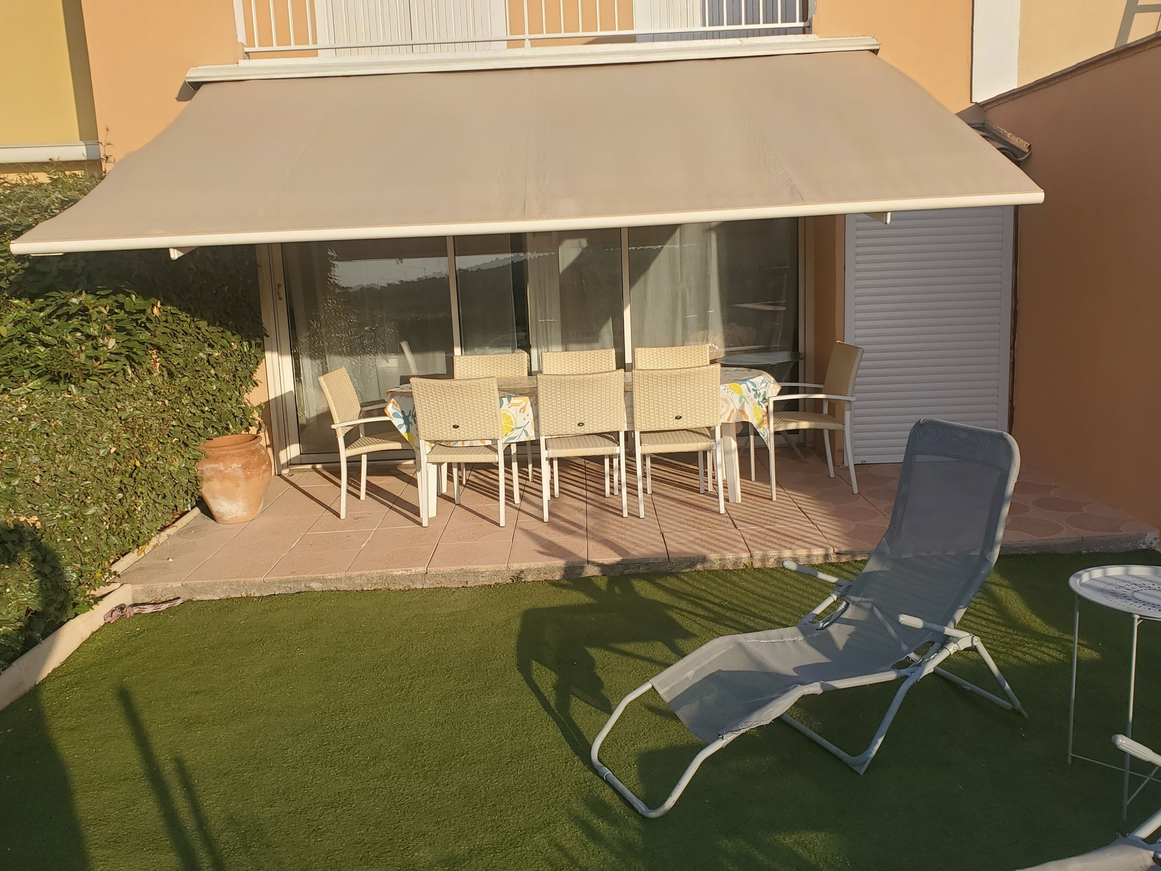 Een terras met een tafel en stoelen, een lounge stoel en een grote parasol.