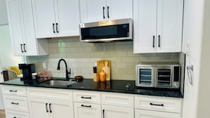 A modern kitchen with white cabinets, a stainless steel microwave, a toaster oven, and a black countertop. - Deluxe Country Cabin - Pet Friendly  (Hot Springs)
