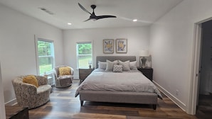 A bedroom with a bed, two chairs, a ceiling fan, and large windows. - Deluxe Country Cabin - Pet Friendly  (Hot Springs)