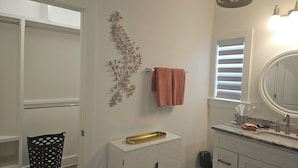 A bathroom with a white vanity, a mirror, a towel rack, and a decorative wall piece. - Deluxe Country Cabin - Pet Friendly  (Hot Springs)