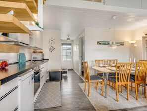 A modern kitchen with white cabinetry, a dining area with wooden chairs, and a visible door leading to another room. - "Melvin" - 50m to the fjord by Interhome (Vestervig)