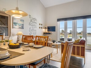 Un comedor con una mesa blanca, sillas de madera, una cesta de fruta y una pared con texto inspirador.