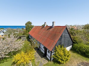 Ein Küstenhaus mit rotem Dach, weißen Wänden und einem Garten mit blühenden Bäumen.