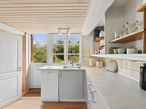Eine moderne Küche mit eingebautem Geschirrspüler, einem Fenster mit Blick auf Grünflächen und einem Regal mit Gläsern.