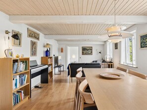 Ein großzügiger Wohnbereich mit Klavier, Bücherregalen, einem Esstisch und einer Couch.