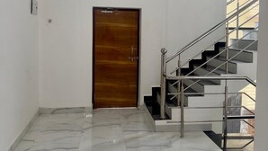 Un couloir avec une porte en bois, un escalier avec des rampes en métal et un sol carrelé.