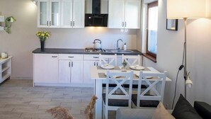 Una cocina moderna con armarios blancos, una zona de comedor con una mesa y sillas, y una lámpara de pie.