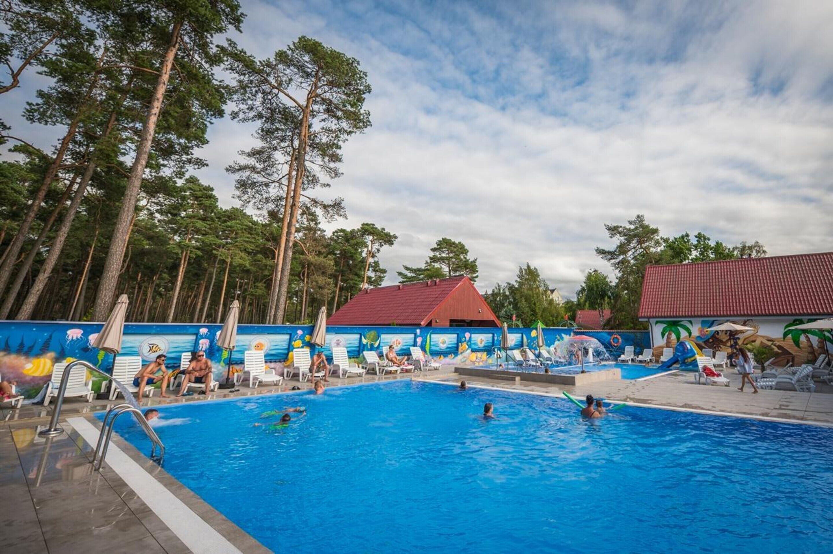 A swimming pool with lounge chairs and a mural, surrounded by tall trees.