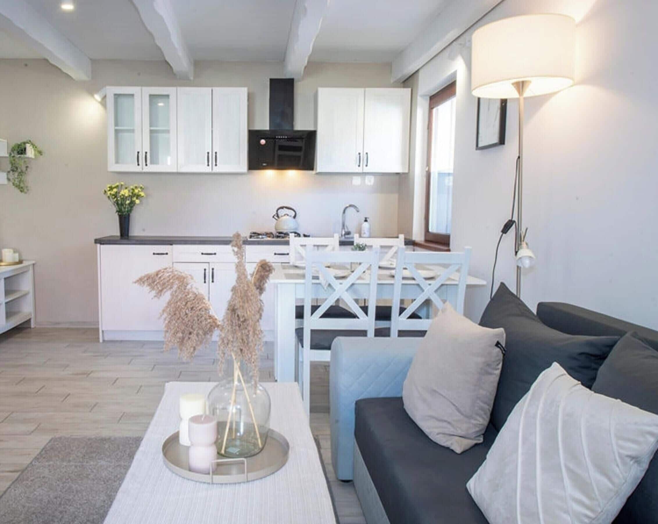 A modern kitchen with white cabinets, a dining table, and a sofa in a living area.
