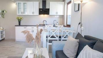 A modern kitchen with white cabinets, a dining table, and a sofa in a living area.