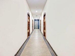 Un largo pasillo estrecho con suelo de baldosas, paneles de madera en las paredes y una puerta de cristal al final.