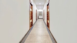Un largo y estrecho pasillo con paredes blancas y piso de baldosas, que conduce a una puerta al final.