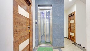 Un pasillo con puertas de madera, un muro de mármol y un ascensor.