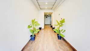 Een gang met houten vloer, aan weerszijden plantenpotten en een plafond met inbouwverlichting.
