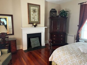 A bedroom with a fireplace, a large cabinet, a bed, and a mirror.