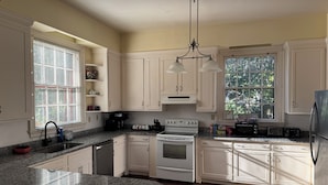 Una cocina con armarios blancos, encimera de granito, estufa, fregadero y refrigerador.