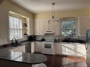 Una cocina con armarios blancos, encimera de granito, estufa, fregadero y refrigerador.