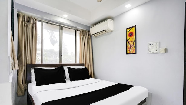A hotel room with a bed, curtains, an air conditioning unit, a painting, and electrical outlets. - Collection O Andheri Near Mumbai Airport (Mumbai)
