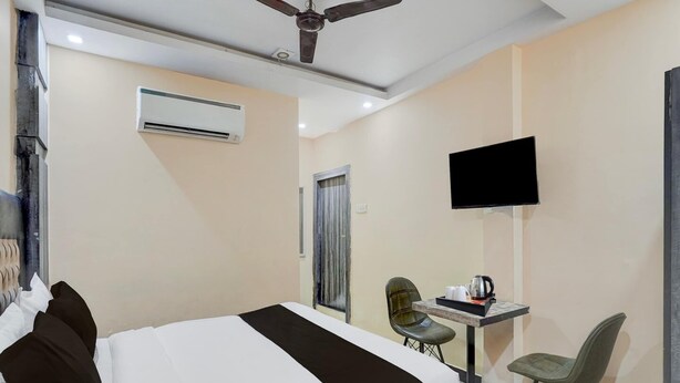 A hotel room with a bed, a desk with a chair, a television, and an air conditioning unit. - Super Deluxe Roomamba Palace (Prayagraj)