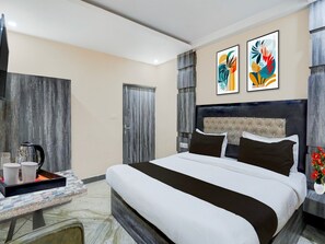 A modern hotel room with a bed, a coffee table with cups, a door, and abstract art on the wall. - Super Deluxe Roomamba Palace (Prayagraj)
