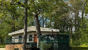 A single-story house with a porch, surrounded by trees and a fenced yard.