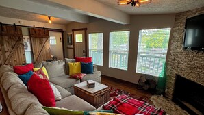 A cozy living room with a sectional sofa, a fireplace, and large windows.