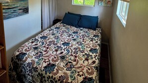 A bedroom with a bed, a ceiling fan, two windows with blinds, and a painting on the wall.