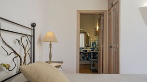 A bedroom with a bed, a bedside lamp, a decorative wall piece, and a view into a bathroom with a mirror and tiled walls. - Villa Junia by Klodge, pool & seaview in San Pantaleo (San Pantaleo)