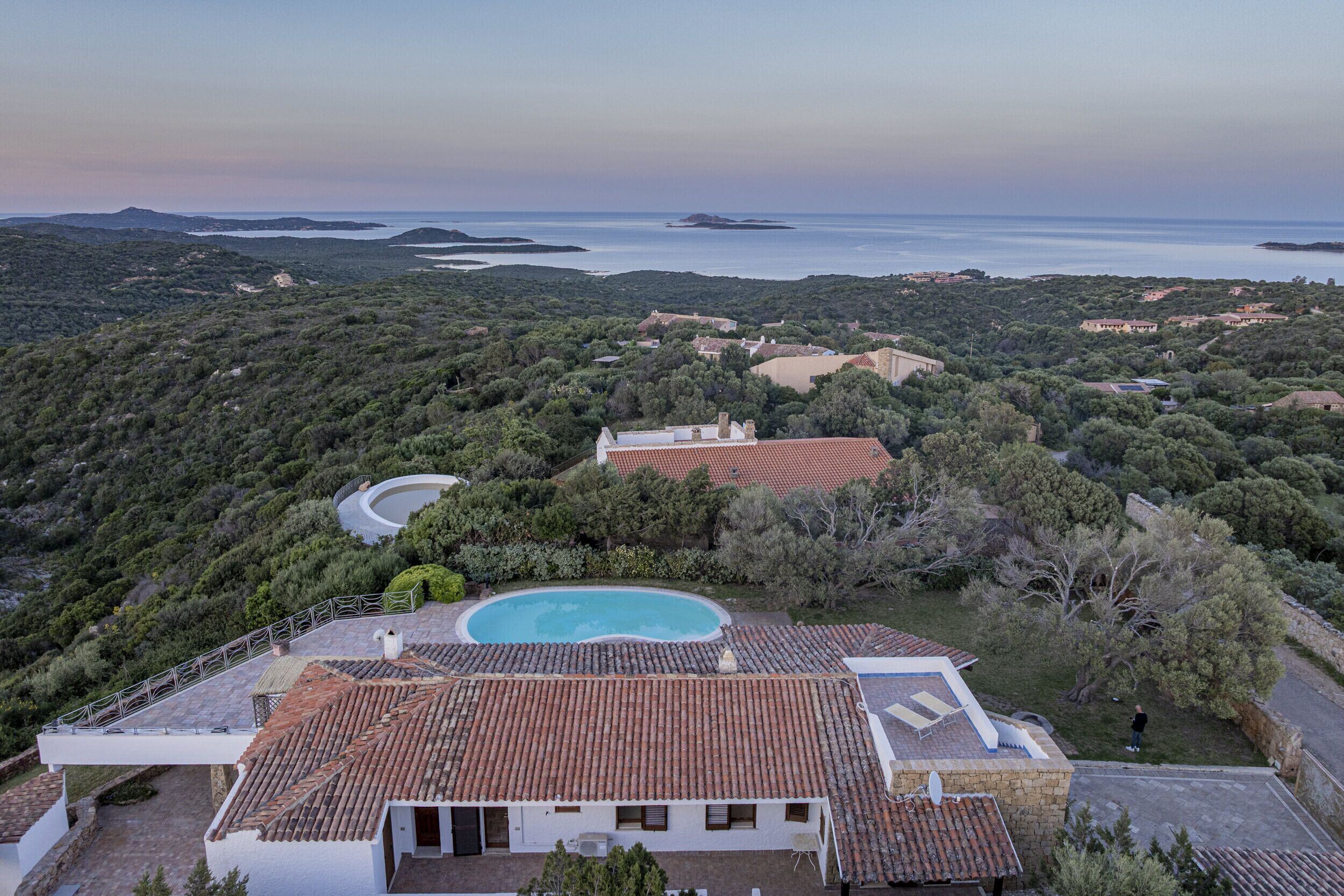 En villa med swimmingpool, omgivet af frodig vegetation med udsigt over et kystlandskab.