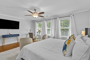 Ein Schlafzimmer mit Bett, Schreibtisch, Stuhl, Deckenventilator und einem an der Wand befestigten Fernseher.