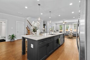 Une cuisine moderne dotée d’un îlot central, de meubles de couleur sombre et de luminaires suspendus.