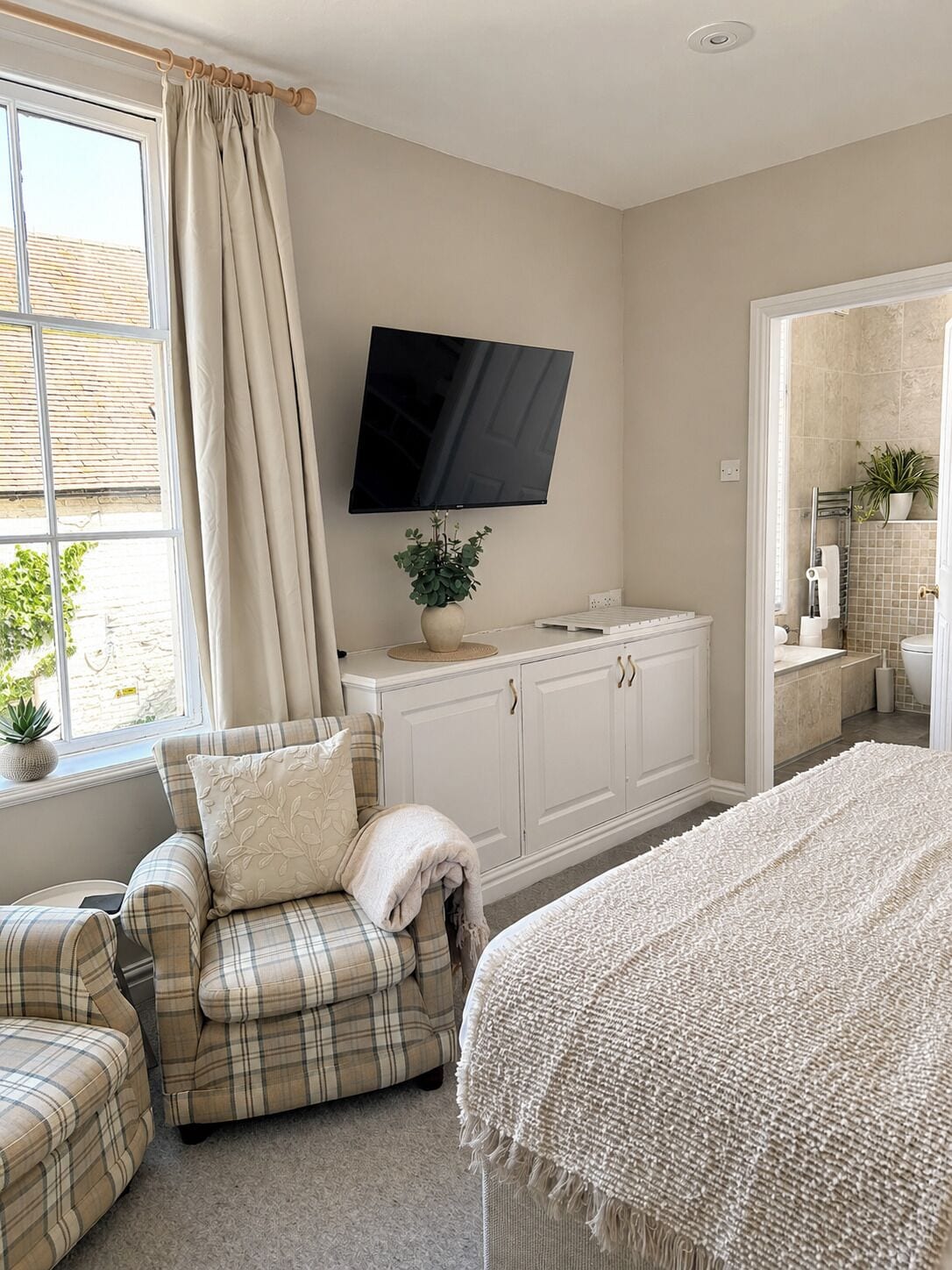 A bedroom with a bed, a TV, a sofa, a cabinet, and a bathroom visible through an open door.