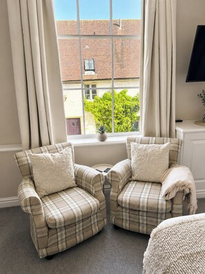 A room with two armchairs, a small table, a window with curtains, a potted plant, and a television on a stand. - Raven Suite - 6 | Central Location (Shropshire)
