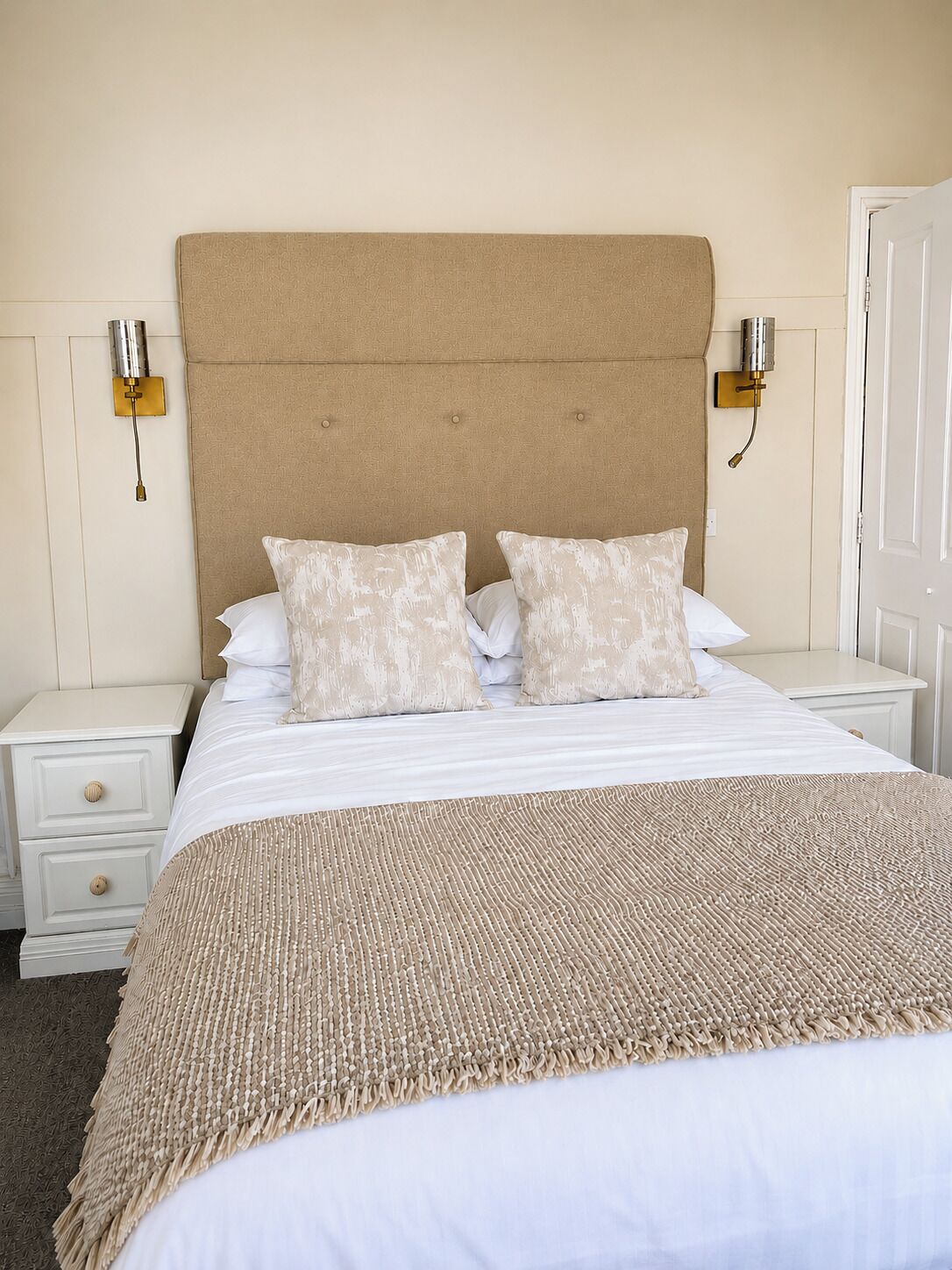 A bedroom with a large bed, two bedside tables, a headboard, and wall-mounted lamps.