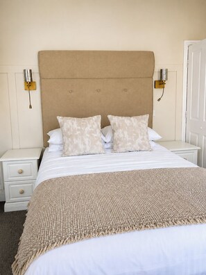 A bedroom with a large bed, two bedside tables, a headboard, and wall-mounted lamps. - Raven Suite - 6 | Central Location (Shropshire)