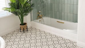 Un baño con bañera, ducha, baldosas de suelo estampadas, una planta en maceta y una ventana con persianas.