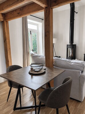 A modern living room with a wooden table, two chairs, a sofa, and a black stove. - The Coach House | Central Location (Shropshire)