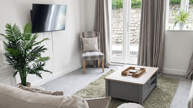 Een moderne woonkamer met een bank, een fauteuil, een salontafel, een televisie en uitzicht door een glazen deur.