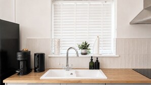 Een keuken met een witte spoelbak, een houten aanrechtblad en grijze kastjes.