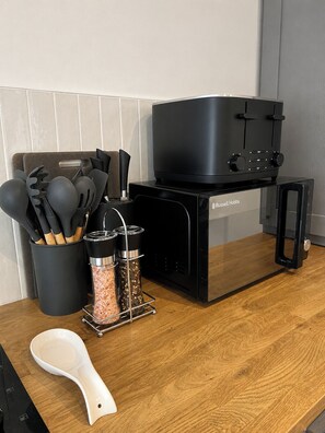 Una cocina con una estufa Russell Hobbs negra, un escurridor de especias y una espátula blanca sobre una encimera de madera.