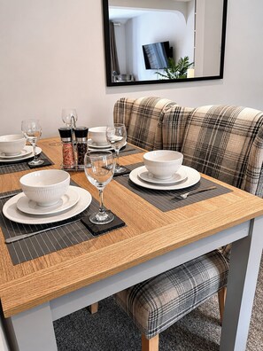Un comedor con una mesa lista para cuatro personas, un sofá y un espejo en la pared.