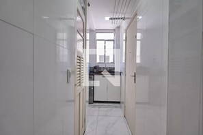 A narrow hallway with white tiled walls and a kitchen area visible through an open door. - Maracanã Comfort. Ideal for families and students. 5 minutes from UERJ and Maracanã. (Rio de Janeiro)